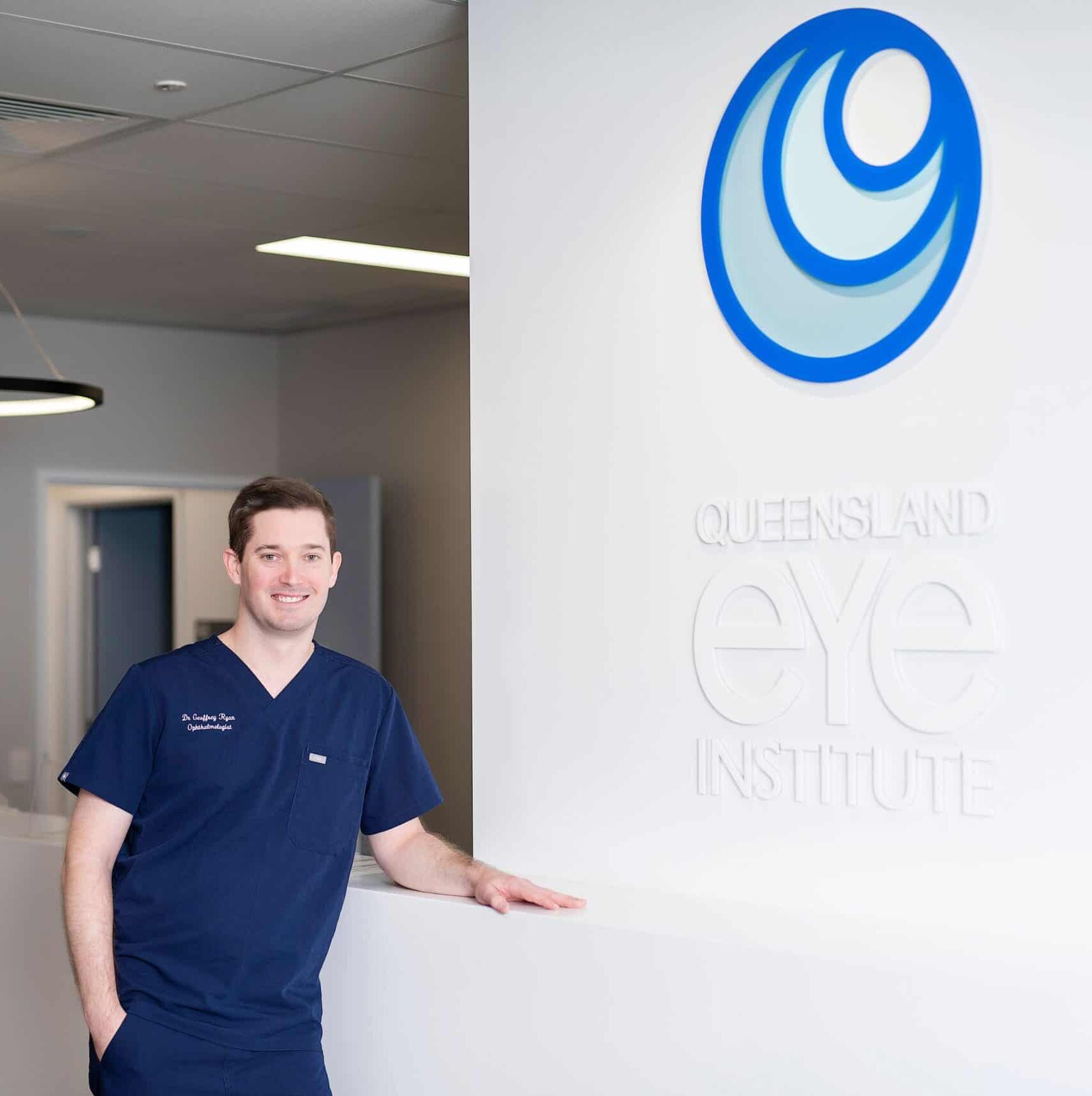 Dr Geoffrey Ryan smiling next to a logo for the Queensland Eye Institute