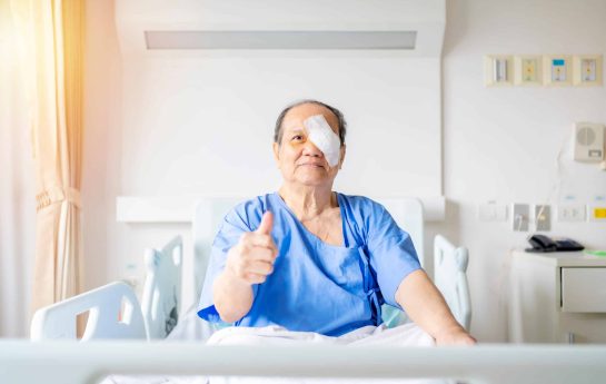 Post eye surgery and patient sitting in bed giving a thumbs up to the camera with an eye patch on.