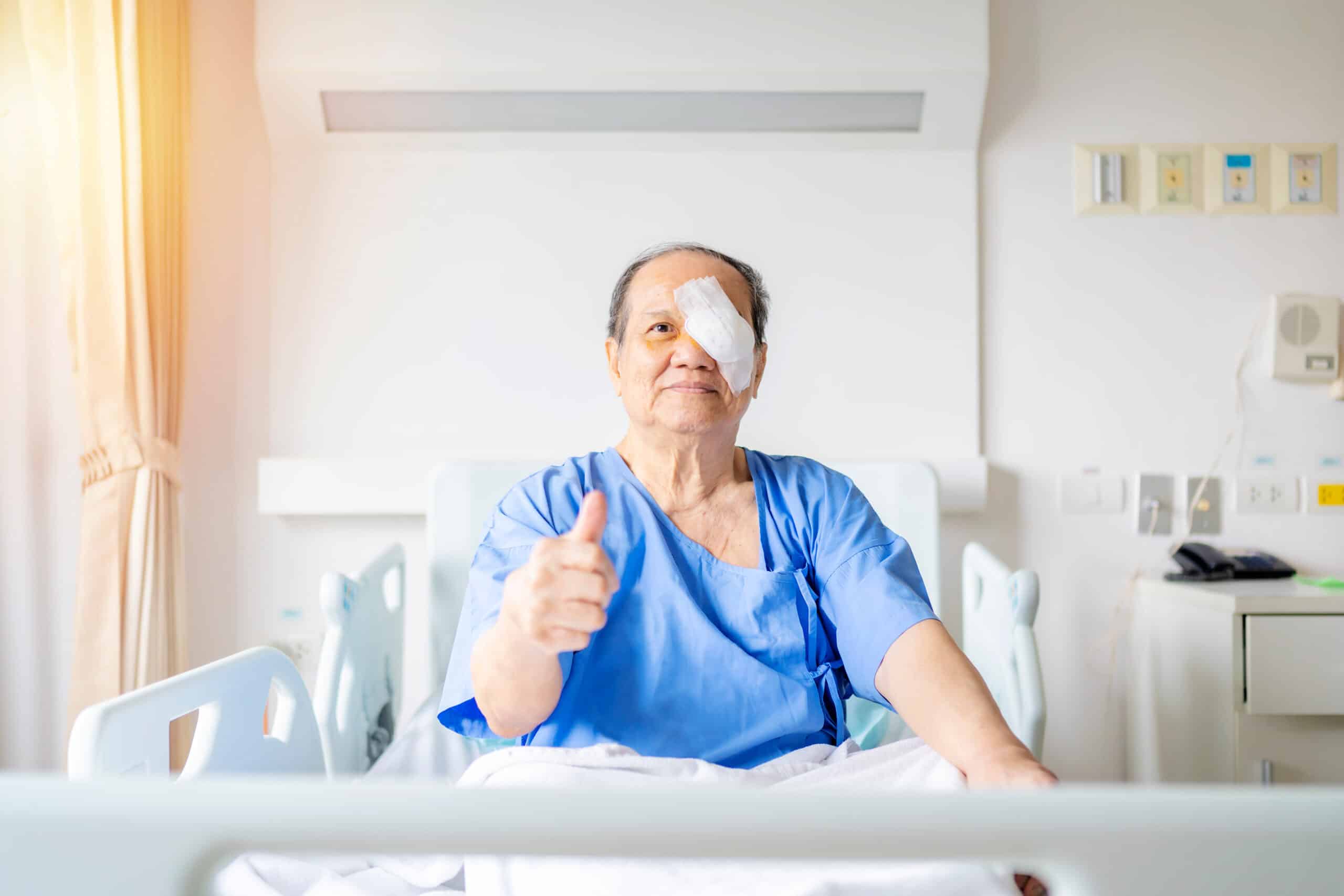 Post eye surgery and patient sitting in bed giving a thumbs up to the camera with an eye patch on.